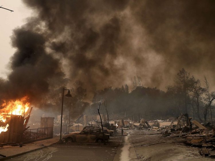 Burned out cars sit next to a building on fire in a fire ravaged neighborhood, Oct. 9, 2017, in Santa Rosa, Calif.
