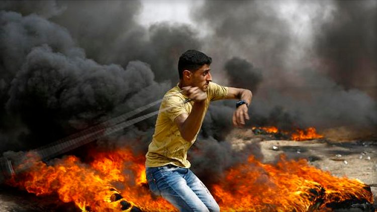 A Palestinian slings a shot by burning tires during clashes with Israeli forces across the border, following a demonstration calling for the right to return � meaning Palestinian refugees being allowed to go back to the land they fled or were expelled from during the 1948 war surrounding Israel's creation � near the border with Israel, east of Gaza City, in the southern Gaza Strip, on April 20, 2018.  MOHAMMED ABED / AFP/GETTY IMAGES