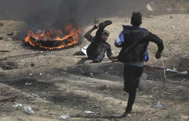 A Palestinian man runs to help an injured protester shot by Israeli troops during a protest at the Gaza Strip's border with Israel, Friday, May 11, 2018. Gaza activists burned tires near the sealed border with Israel on Friday in a seventh weekly protest aimed at shaking off a decade-old blockade of their territory. Israeli soldiers fired tear gas volleys from the other side of the border fence. (AP Photo/Khalil Hamra)