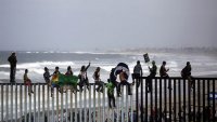 Central American migrants straddling U.S./Mexico border fence between San Diego and Tijuana