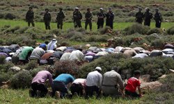 Palestinians praying near Israeli soldiers, protesting land confiscation in the village of Qusra, near Nablus